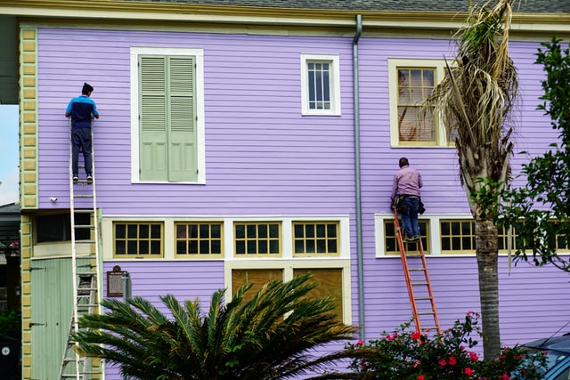 2 men on ladders painting the siding of a house